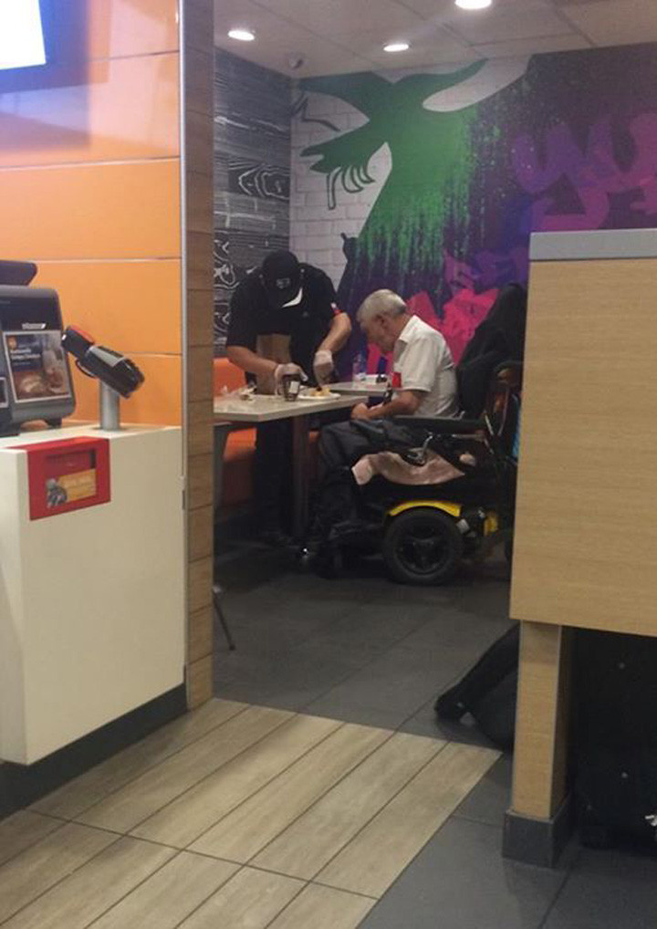 An employee of McDonald's helping a disabled elderly man eat his meal.