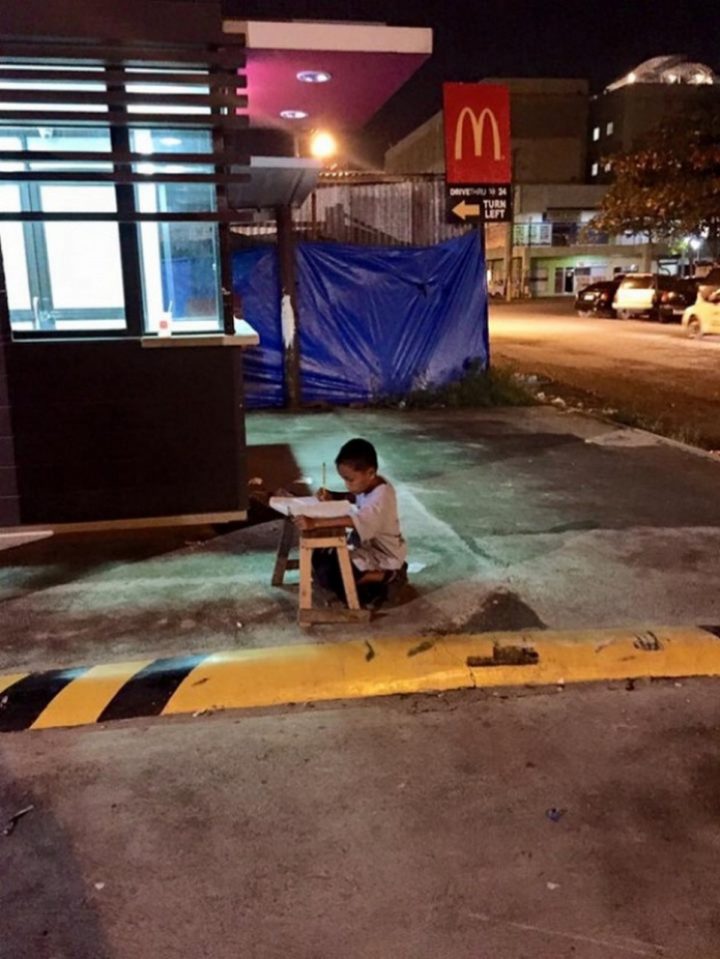 9-year-old Daniel Cabrera completing his homework on a makeshift desk on the pavement and using faint light from a nearby McDonald’s restaurant.