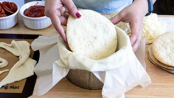 Now that you have 5 baked pizza crusts, line the inside of the pan with parchment paper and drape the long strip of dough around the inside of the pan leaving an overhang as shown. Put the first piece of cooled pizza dough at the bottom of the pan.